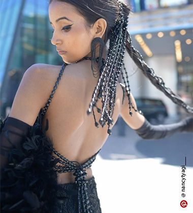 Nancy Tyagi wearing a black corset top, a skirt with a train, and a fur scarf at the 77th Cannes Film Festival Red Carpet