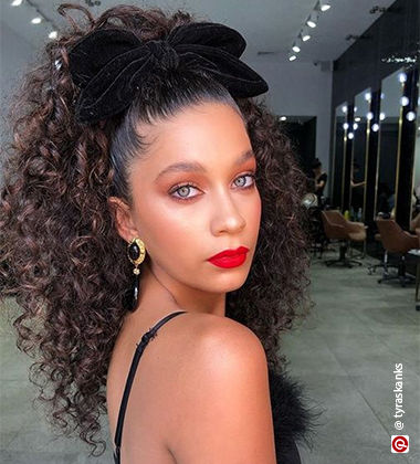 WOman looking over her shoulder with a black bow on her curly ponytail