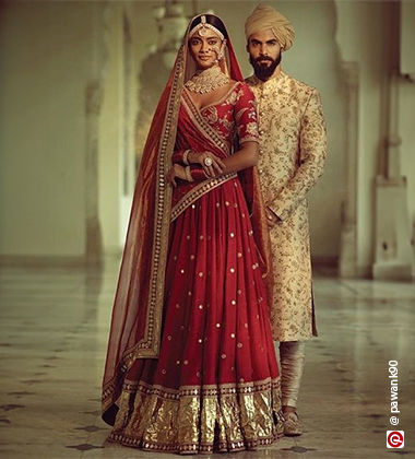 Woman wearing red lehenga with the groom standing behind her